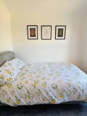 A bed with a lemon pattern bedspread, a grey headboard, and three framed motivational quotes on the wall. - Room-spacious Double Room-parking-self C (Grays)
