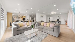 A spacious living area with a grey sectional sofa, a white coffee table, and a grey shag rug.