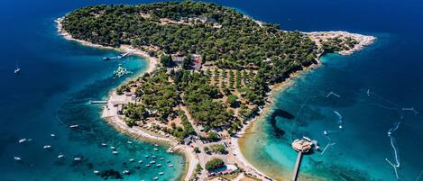 An aerial view of a coastal town with clear blue waters, a small island with dense greenery, and a few buildings near the shore.
