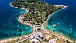 Luftaufnahme einer Küstenstadt mit klarem, blauem Wasser, einer kleinen Insel mit üppiger Vegetation und einigen Gebäuden in der Nähe des Ufers.