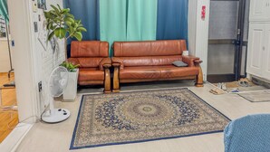 A living room with a brown leather sofa, a white fan, a patterned rug, and a blue and green curtain. - 3BR Seongsu Station 3min walk Urban Cozy House2 (Seoul)