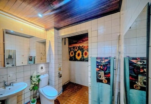 A bathroom with white tiles, a sink, a toilet, and a shower area.
