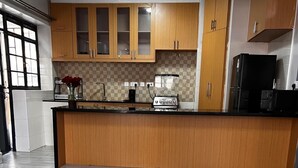 A modern kitchen with wooden cabinets, a black refrigerator, and a tiled backsplash. - Unimash Homes Kenya W/SwimmingPool Available For Long/Short Term Stays (Nairobi)