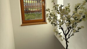 Un escalier avec une rampe en bois, une fenêtre donnant sur une clôture en bois et des montagnes, et une plante à fleurs blanche en pot.