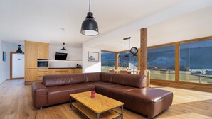 Un salon moderne avec un canapé en cuir marron, une table basse en bois et une grande fenêtre donnant sur un champ.