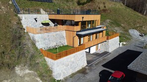 A modern two-story building with a stone base and wooden upper levels, featuring balconies and a paved driveway. - Exclusive mountain chalet | Private sauna | Breathtaking glacier panorama (Neukirchen am Großvenediger)