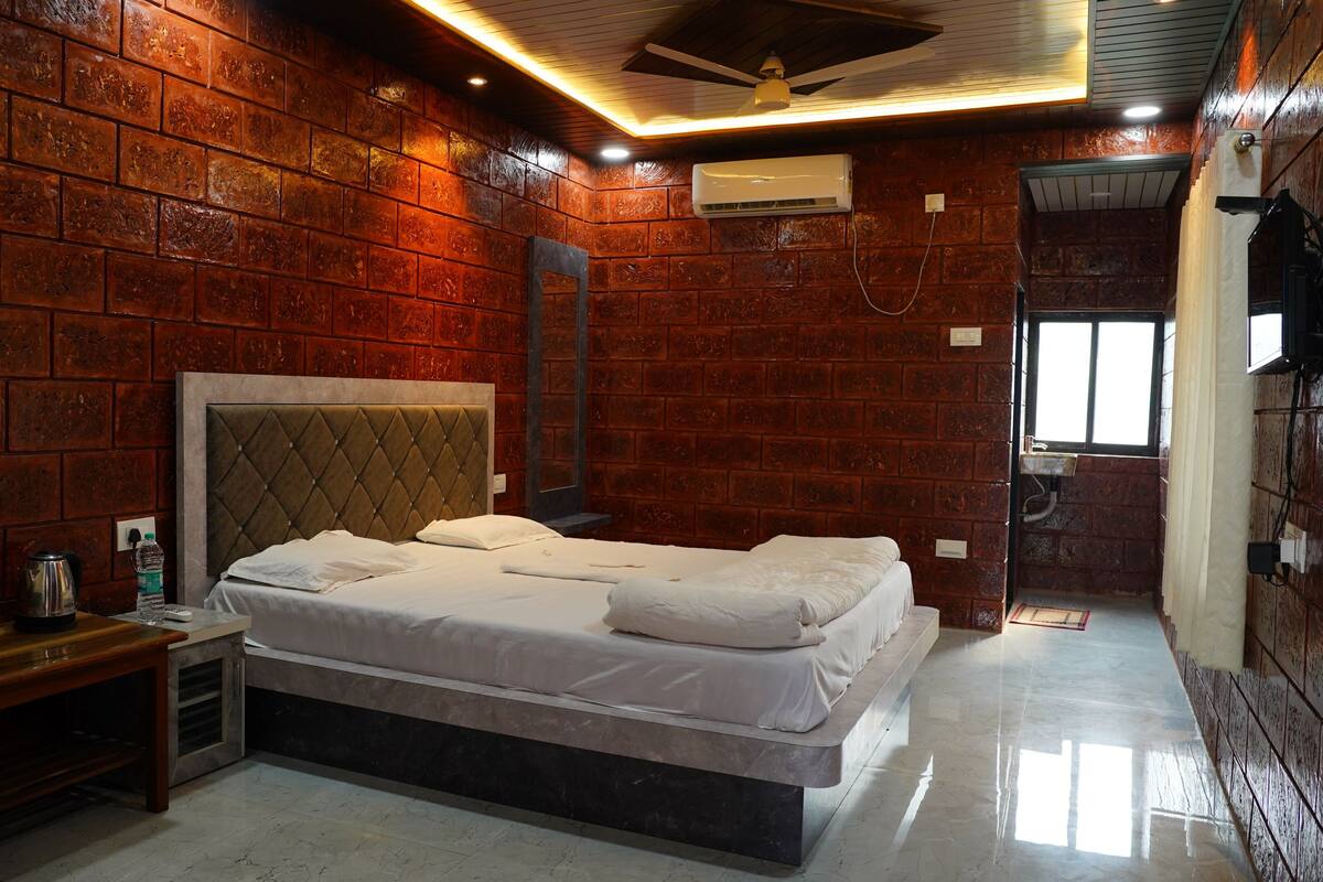 Una habitación con pared de ladrillo, cama con ropa de cama blanca, banca de madera y ventilador de techo.