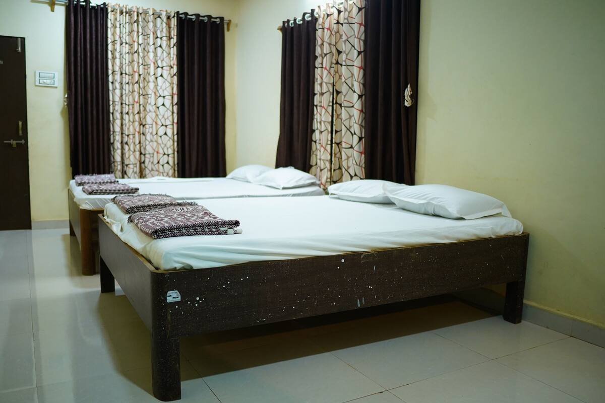Habitación con tres camas, cada una con sábanas blancas y almohadas estampadas, cabecero de madera oscura y cortinas de diseño geométrico.