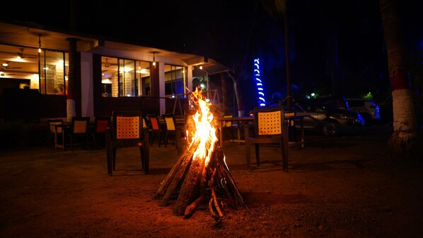 A fire pit in the foreground with chairs and tables arranged around it. - Swapnali Beach Resort (Murud)