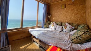 Een houten kamer met een bed, een raam met uitzicht op zee en een hanglamp.