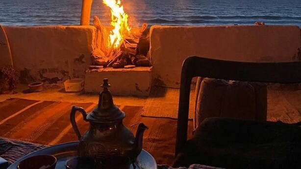Een gedekte tafel met theepot, kopjes en een dienblad, met uitzicht op een haardvuur en de zee.