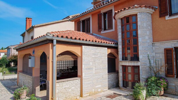 Ein Gebäude mit einer Stein-Fassade, einem Ziegeldach und einer kleinen überdachten Terrasse.