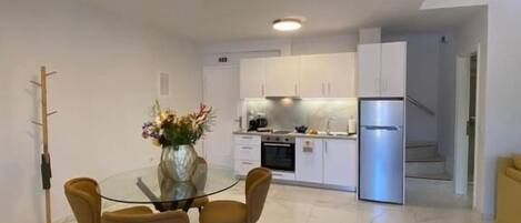 A modern kitchen with white cabinets, a stainless steel refrigerator, and a dining area with a glass table and chairs.