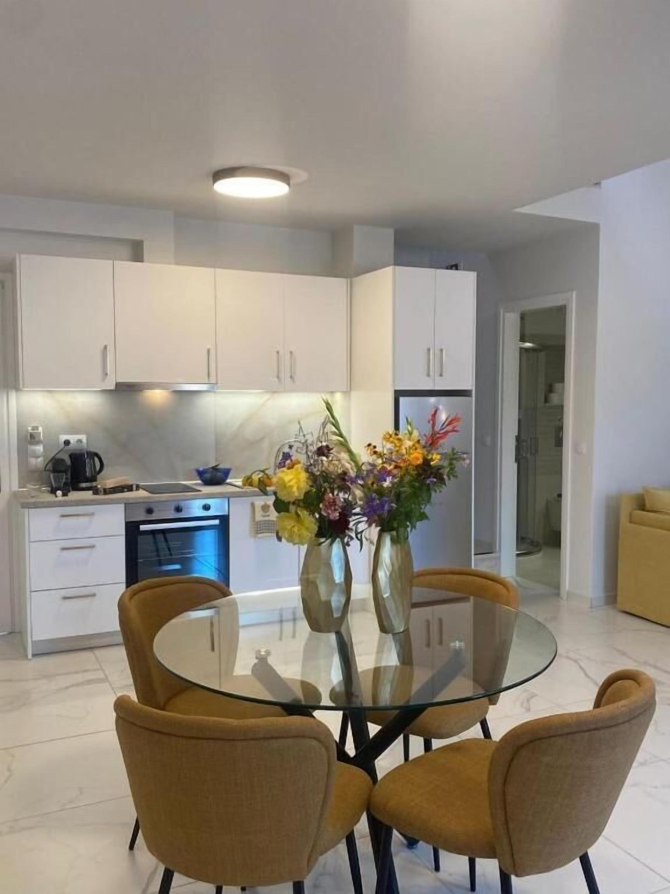 Una cocina moderna con armarios blancos, una mesa de comedor de vidrio y un jarrón de flores.