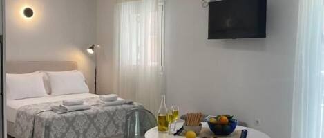 A hotel room with a bed, a round table with chairs, a TV, and an air conditioning unit.
