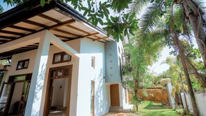 A building with a covered porch, a door, and a small garden area with a pathway. - Spacious 5-bedroom villa near Ragama Teaching Hospital (Kadawatha)