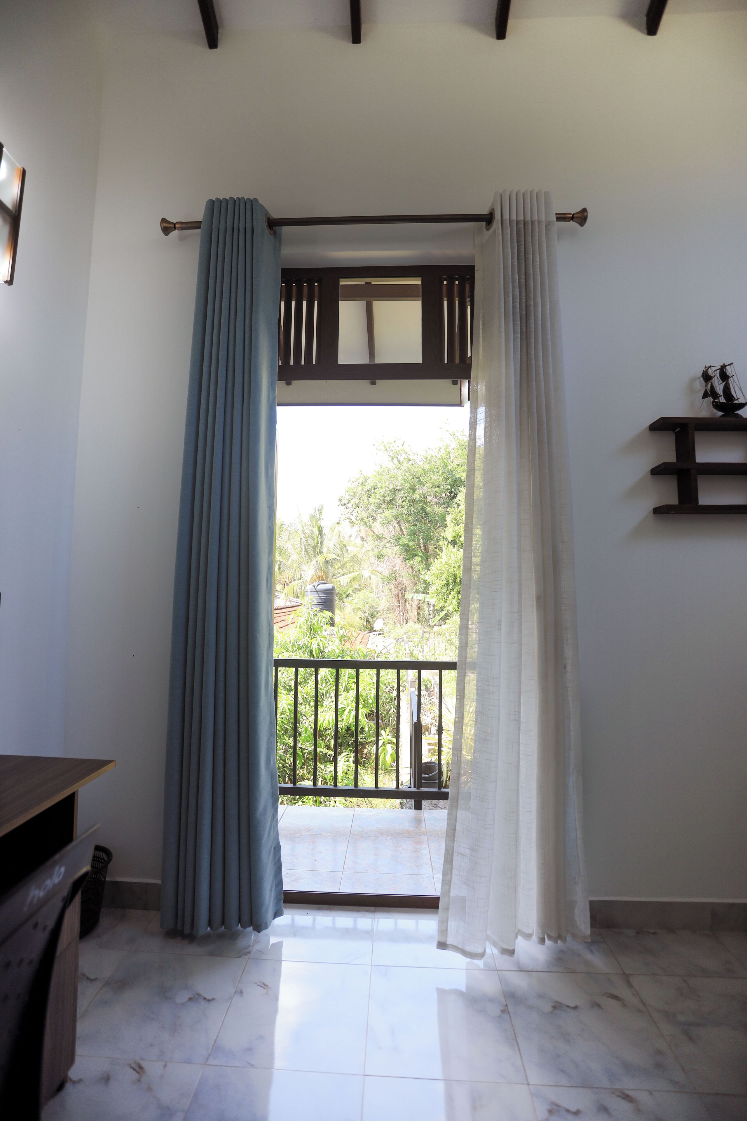 A room with a balcony, a wooden desk, and a tiled floor.