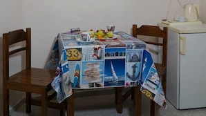 Un comedor con una mesa cubierta con una revista, dos sillas, un refrigerador y una obra de arte floral enmarcada en la pared.