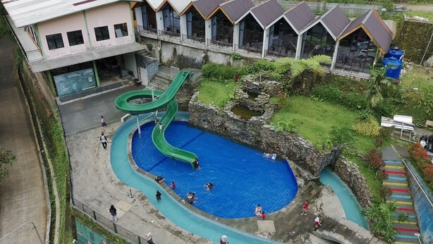 Ein Schwimmbecken mit einer grünen Rutsche, ein Gebäude mit vielen Fenstern und eine Steinstruktur.