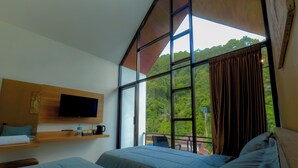 Ein Zimmer mit großem Fenster, einem Flachbildfernseher, einem Bett und einem Regal mit Wasserflasche und Kaffeemaschine.