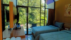 Ein Schlafzimmer mit zwei Betten, einem Schreibtisch mit Flachbildfernseher und einem großen Fenster mit Blick auf Bäume.