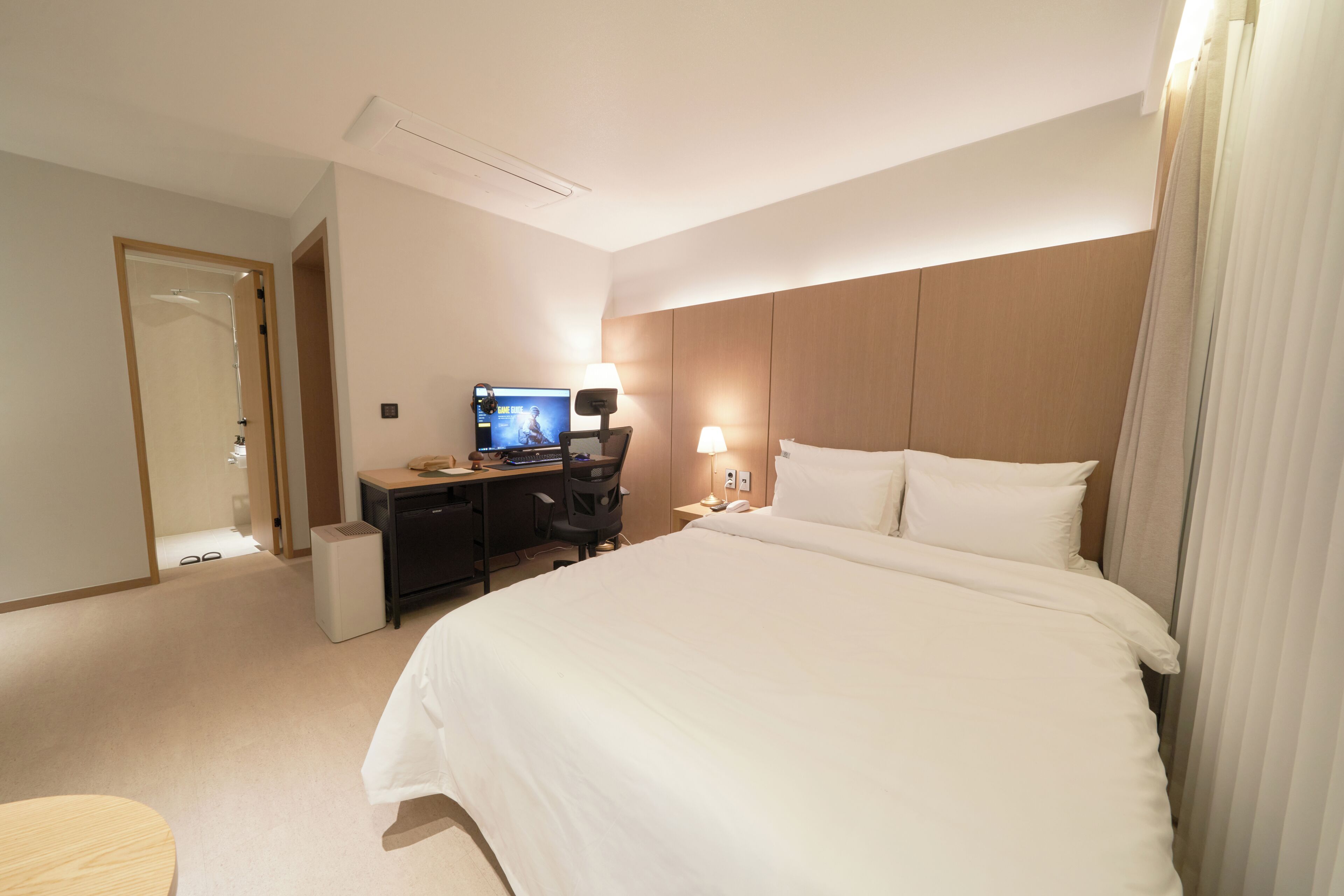 Una habitación de hotel con una cama grande, un escritorio con computadora, televisor y lámpara.