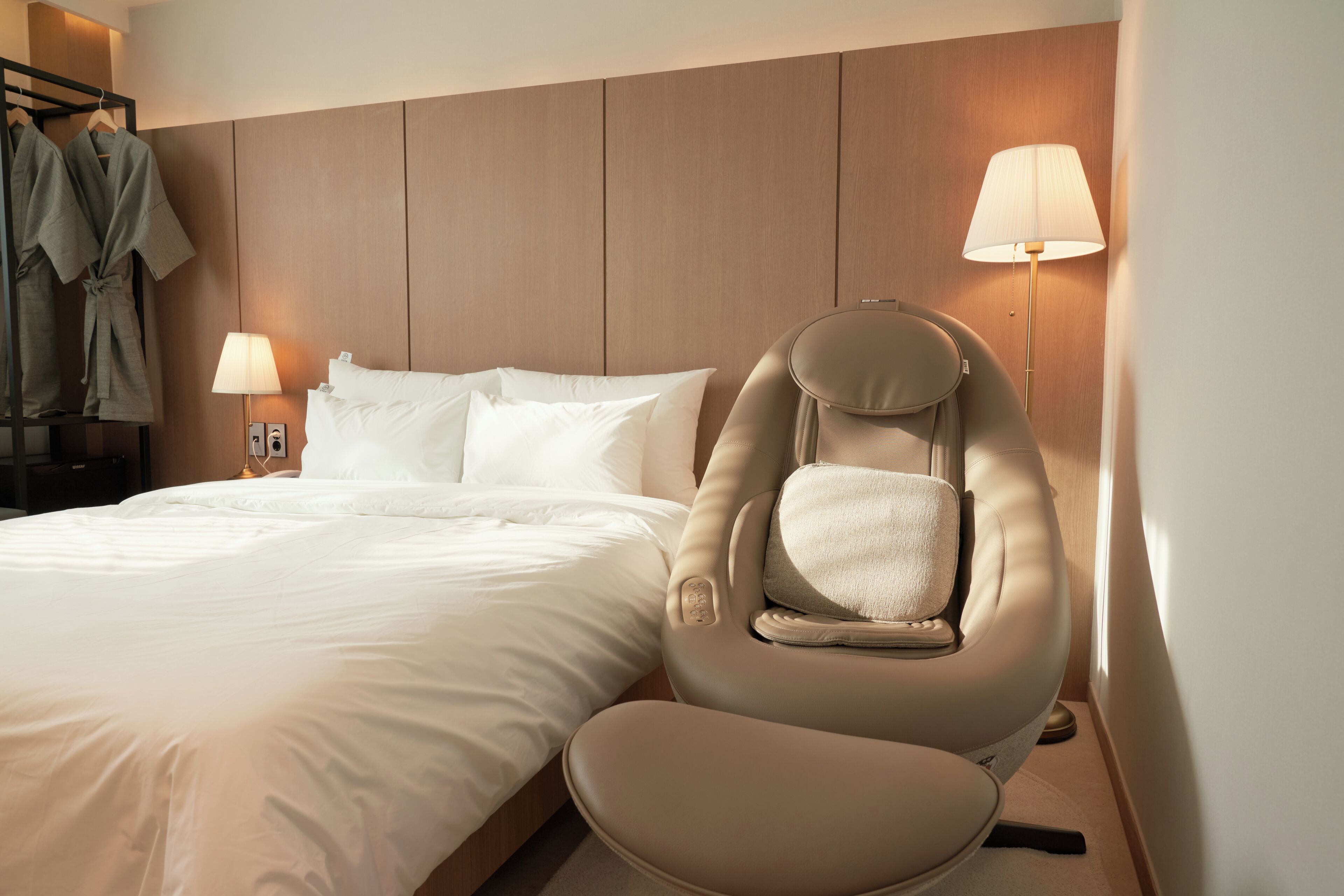 Une chambre d’hôtel équipée d’un lit, d’un fauteuil de massage et de deux lampes de chevet.