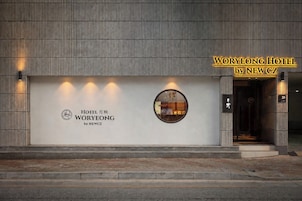 A hotel entrance with a modern facade, a prominent sign for WORYEONG HOTEL by NEWCZ, and a circular window reflecting the interior.