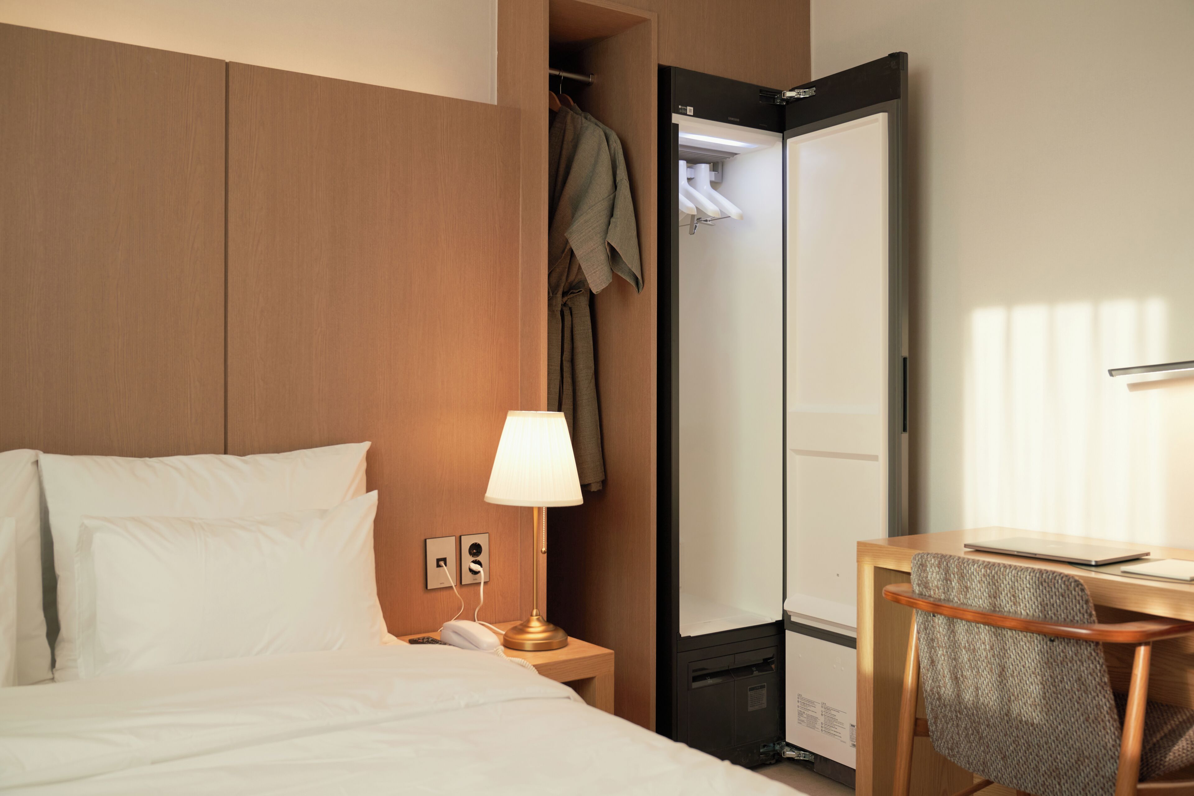 A hotel room with a bed, bedside lamp, desk with chair, and a mirror.