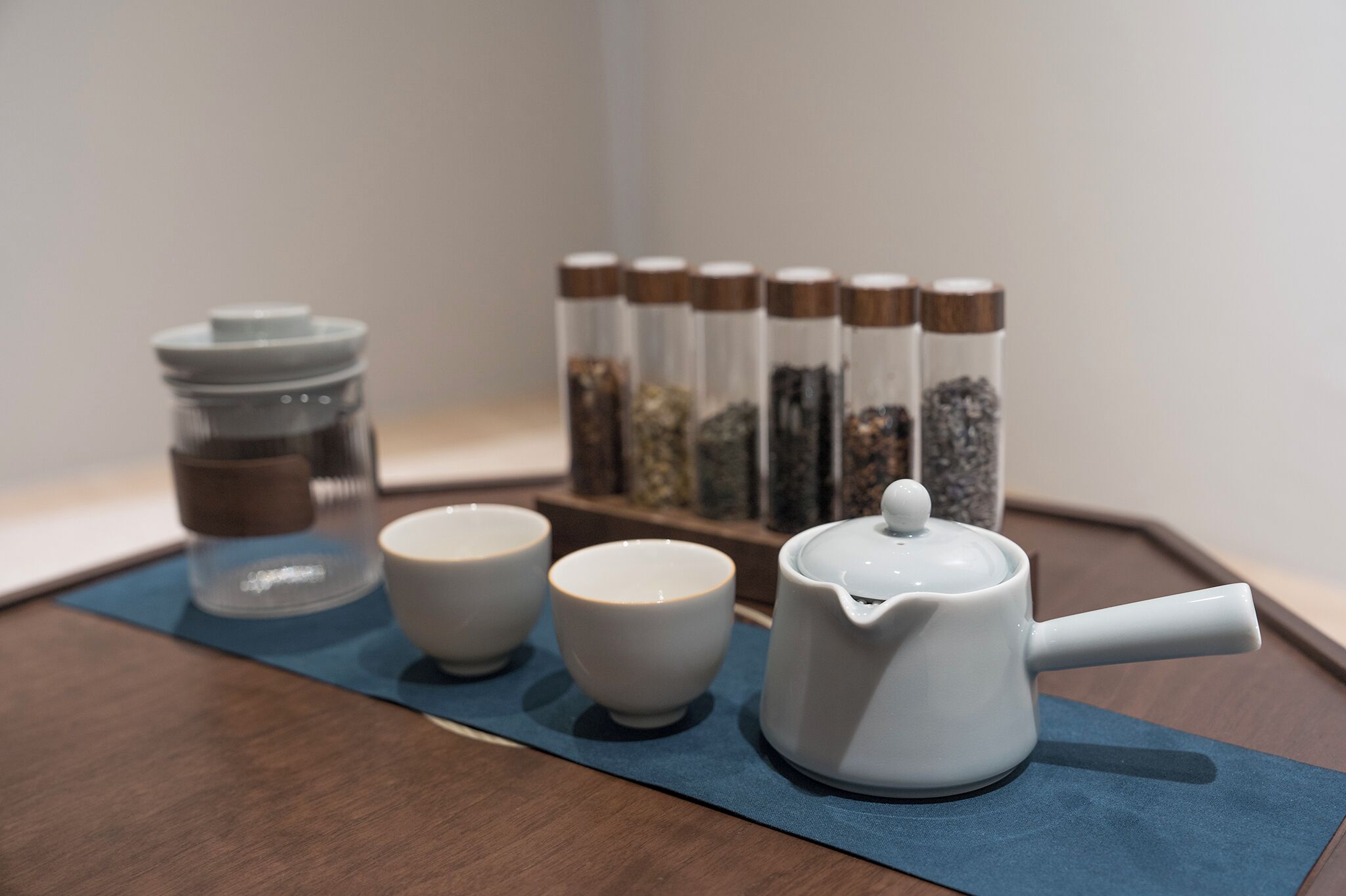 A tea set on a tray with a blue mat, a jar, and spice containers.