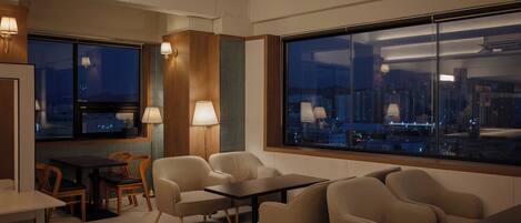 Un interior moderno con una zona de estar, una mesa de comedor y grandes ventanales con vistas a la ciudad.