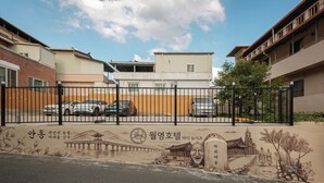A gated parking area with a mural depicting a traditional Korean scene, a modern building with a flat roof, and a clear sky. - Woryeong Hotel By NewCZ (Andong)