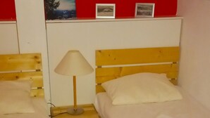 A hotel room with two single beds, a nightstand with a lamp, a red wall with framed pictures, and a striped rug. - Vacation apartment Glockenblume 5 (Siegsdorf)