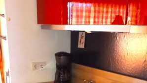 A compact kitchen with white cabinets, a black stove, and a red upper cabinet. - Vacation apartment Glockenblume 5 (Siegsdorf)