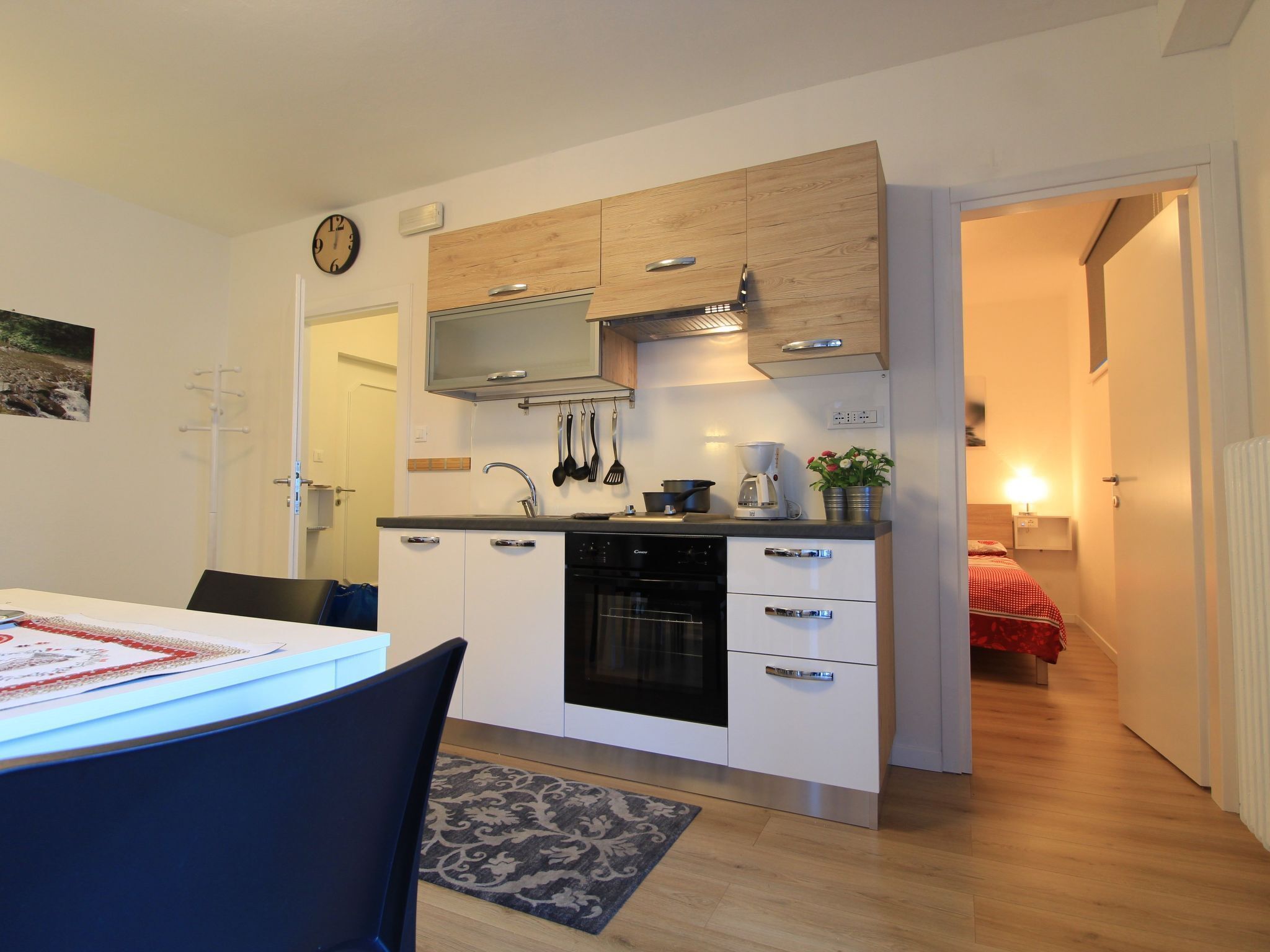 A compact kitchen with white cabinets, a black oven, and a coffee maker. There is a dining table with chairs and a rug.