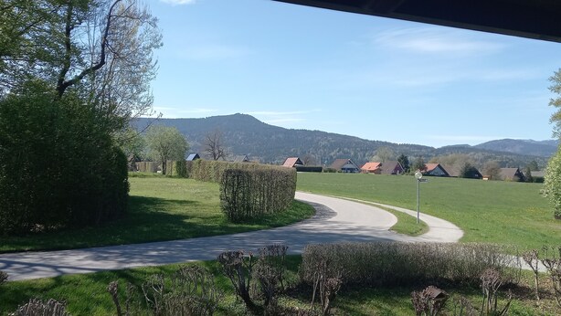 A rural landscape with a winding road, green fields, and houses in the distance. - House Crocus, room no. 12 (Siegsdorf)