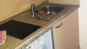 A compact kitchen with a built-in sink, a small refrigerator, and a countertop with a red object. - House Crocus, room no. 12 (Siegsdorf)