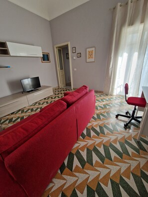 Ein Zimmer mit einer Couch, einem Fernseher auf einem Schrank, einem Sessel und einem gemusterten Boden.