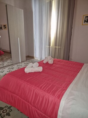 Een hotelkamer met een bed, een spiegel, een deur en een raam met gordijnen.