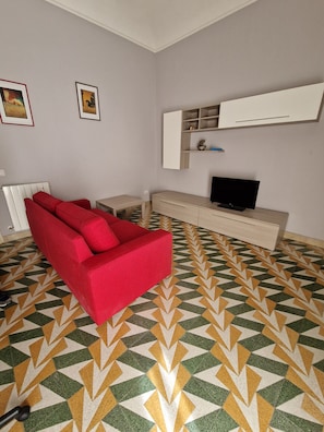 Ein Wohnzimmer mit einem roten Sofa, einem Fernseher, einem wei ßen Schrank und einem fußbodenmuster.