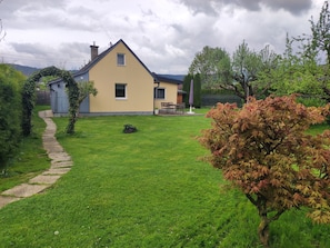 Ett hus med en asfalterad uppfart, en gräsmatta och en trädgårdsdel med träd och buskar.