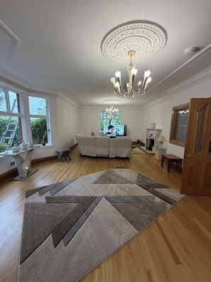 A spacious living room with a large chandelier, a white sofa, and a patterned rug.