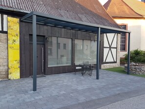 Een overdekt buitenterrein met een modern ontwerp, een houten deur en een geel bord aan de muur.