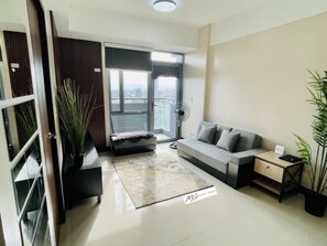 A modern living room with a sofa, a coffee table, a side table, a potted plant, and a large window with a view. - Minimalist 1BR Condo in Araneta City (Quezon City)