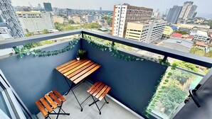 Uma varanda com mesa e cadeiras de madeira, um vaso de planta e vista para a cidade.
