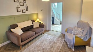 En moderne stue med sofa, gul lænestol, et mønstret tæppe og en hængende lampe.