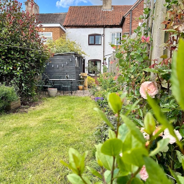 Un jardin avec un abri en bois, une pelouse et une maison en briques surmontée d’un toit en tuiles.