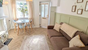 En hyggelig stue med en brun sofa, et spisebord med stole, en gulvtæppe med mønster, og udsigt gennem et vindue.