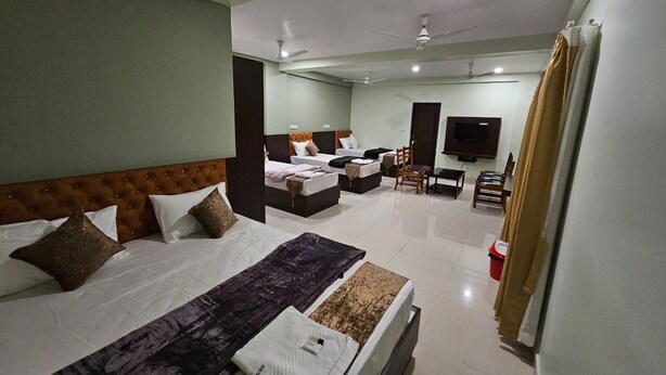 A hotel room with a large bed, a smaller bed, a desk, a chair, a TV, and a ceiling fan. - Hotel Gokarna Palace (Ankola)
