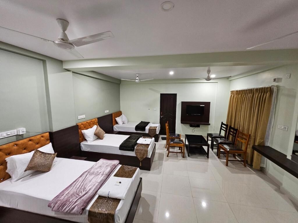 A hotel room with three beds, a TV, a desk, and a chair.